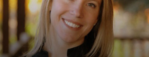 Lisa Osterling is wearing a black jacket. She has shoulder-length blond hair and is smiling in front of a blurry background.
