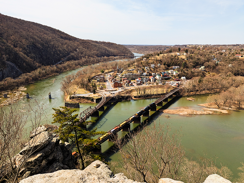 View of Harpers Ferry with a train crossing a bridge over the river.