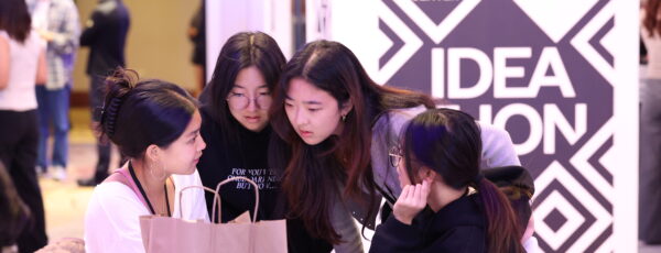 Four Ideathon participants huddle for discussion in front of an Ideathon an banner in the background.
