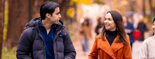 Vice Dean Lamberton and two students walk together on Locust Walk in the autumn, smiling and talking