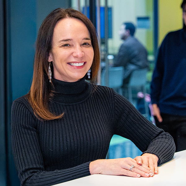 Cait Lamberton in a black turtleneck smiles while at the front desk in the Undergraduate Division.