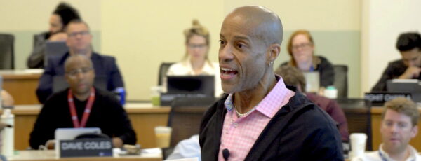 Americus Reed addresses a classroom of students, while holding a document.