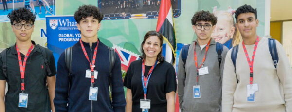 Five people wearing conference lanyards stand in a row to pose for a photo at the Wharton Global Youth Learning Sprint.